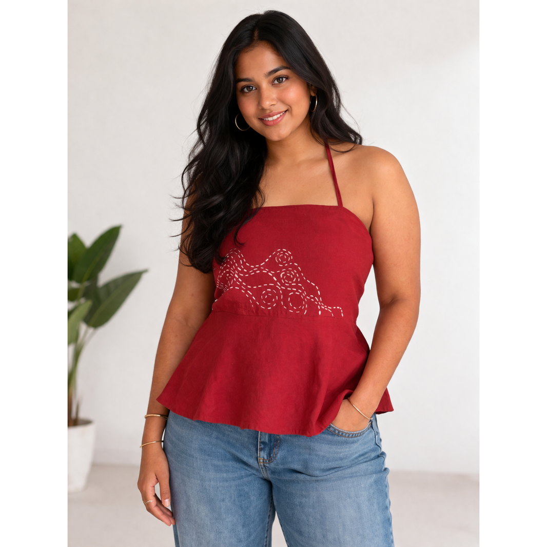 Woman wearing a red peplum halter top with floral embroidery and blue jeans against a white background