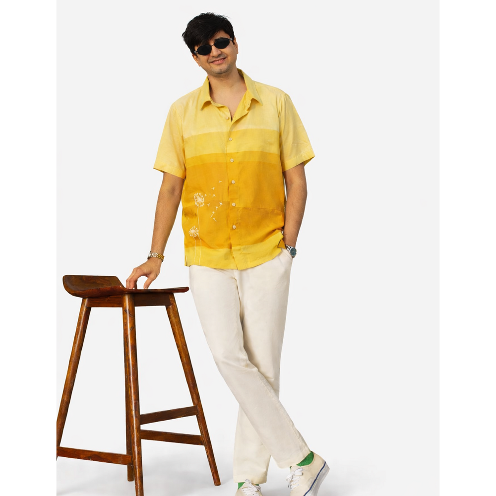 Man wearing a yellow shirt and white pants standing next to a wooden stool on a white background