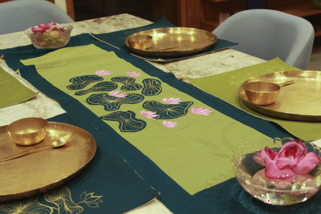 Decorative table setting with green placemats featuring floral designs, gold plates, and pink flowers.