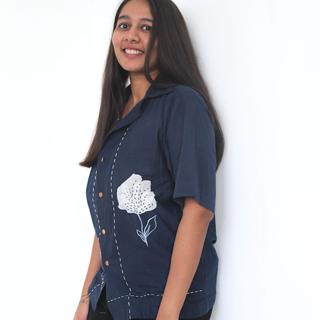Woman wearing a navy blue shirt with white floral embroidery on a white background