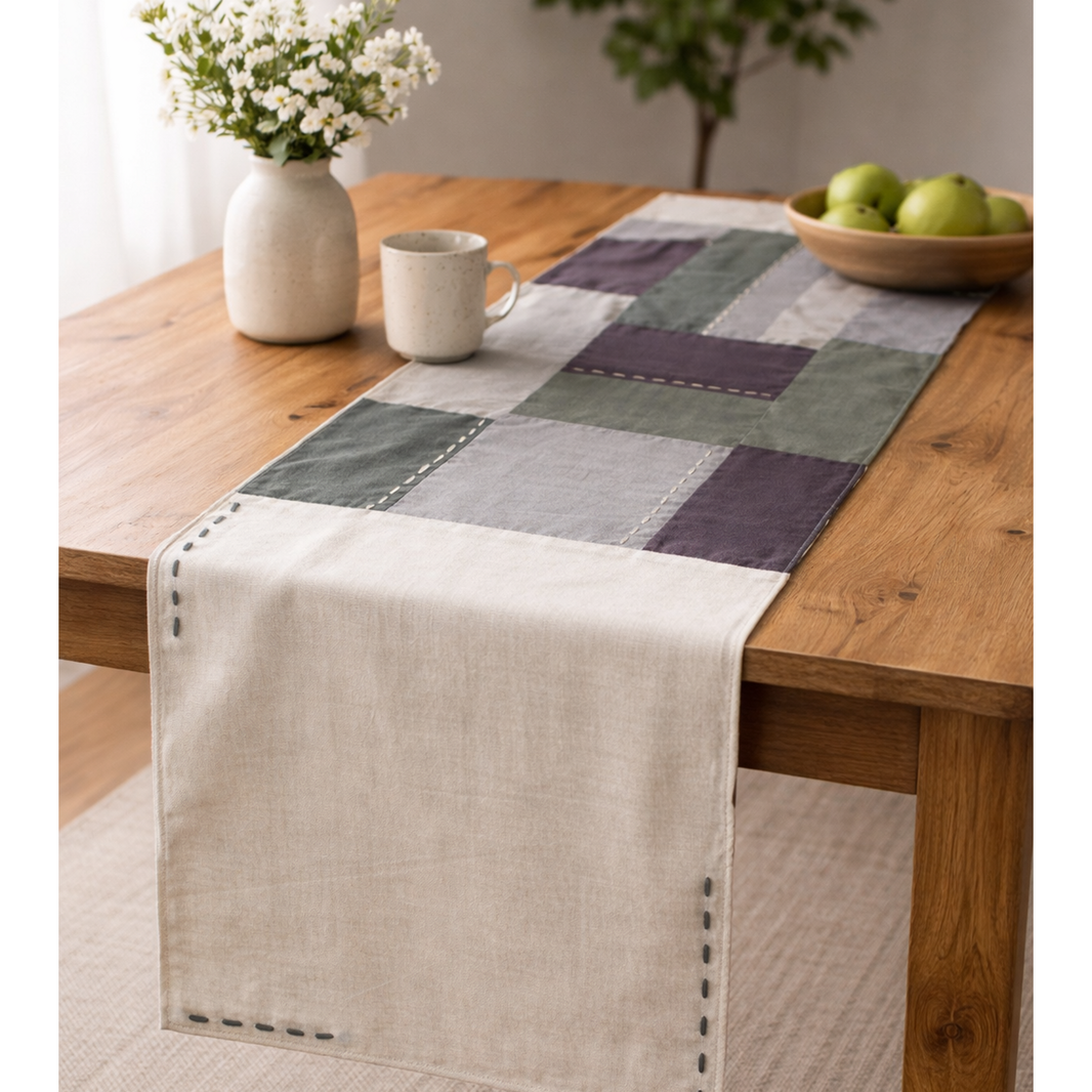 Checkered cotton table runner on a wooden table with a vase, mug, and bowl of apples.