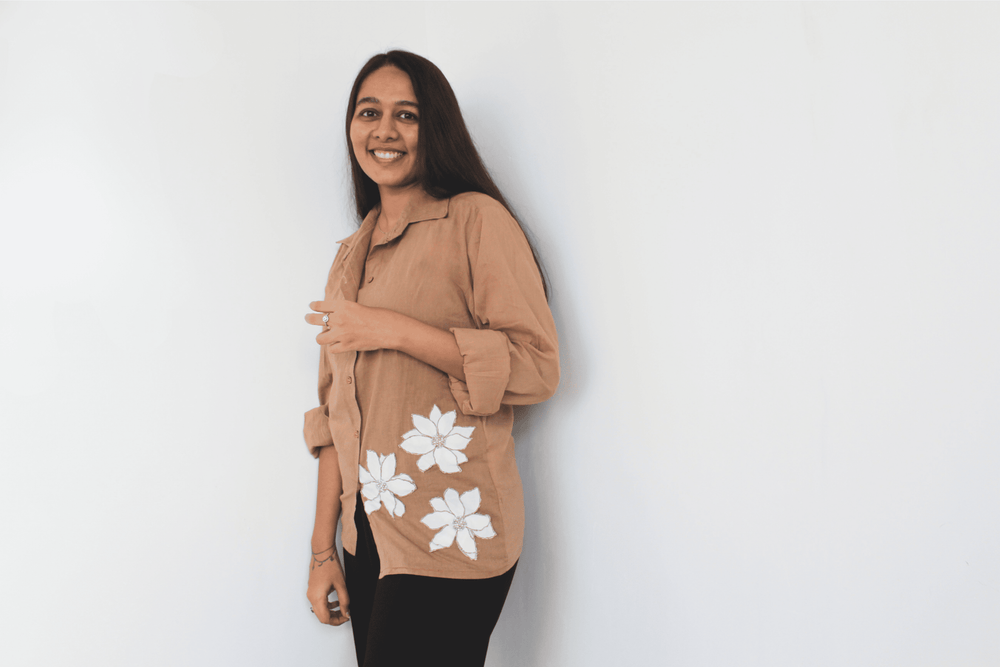 Woman wearing a beige shirt with white floral patterns on a plain background