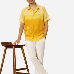 Man wearing a yellow shirt and white pants standing next to a wooden stool on a white background