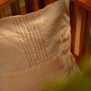 Close-up of a wooden swing with a white and beige pillow featuring intricate stitching.