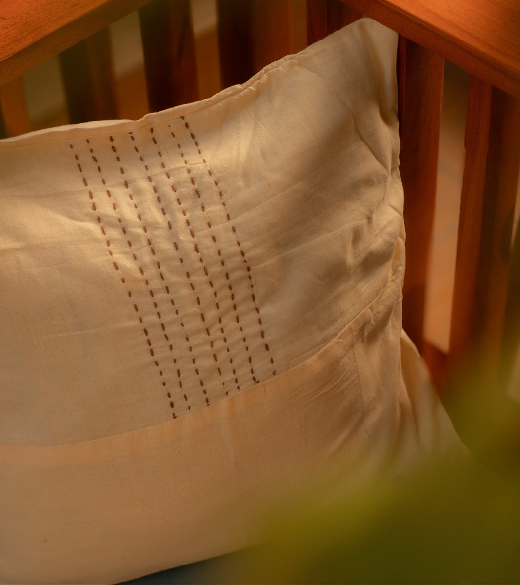 Close-up of a wooden swing with a white and beige pillow featuring intricate stitching.