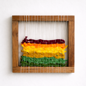 Colorful woven wall art with red, yellow, and green on a wooden frame against a white background