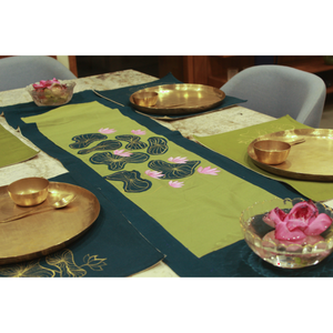 Decorative table setting with green placemats featuring floral designs, gold plates, and pink flowers.