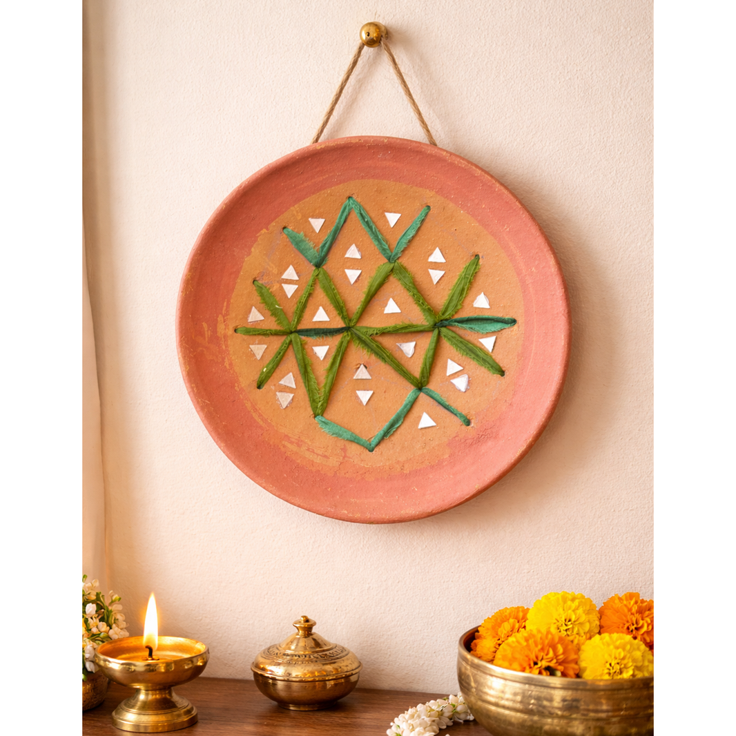 Decorative wall plate with geometric design on a wall with candles and flowers below.