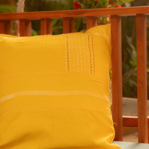 Yellow pillow on a wooden swing with greenery in the background