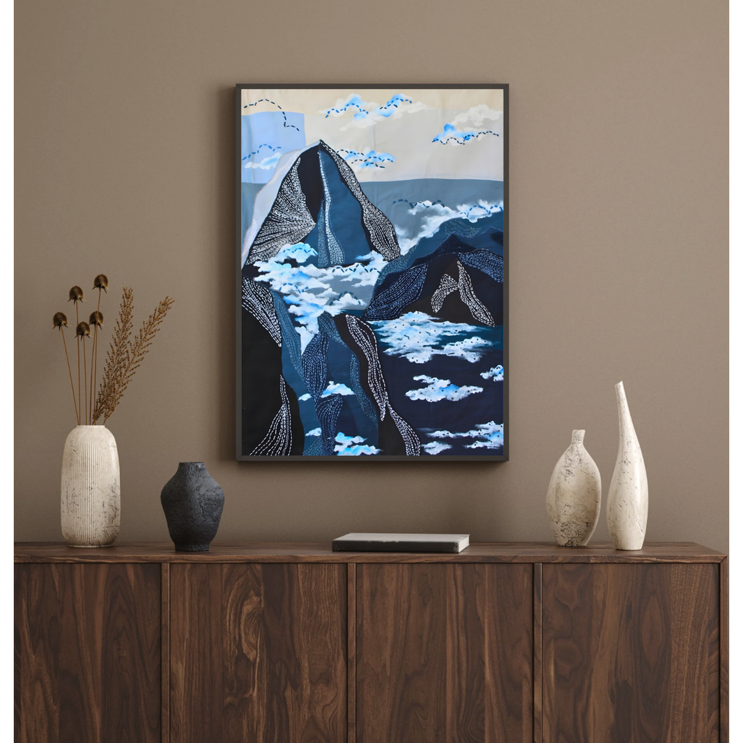 Framed mountain inspired artwork on a wall above a wooden cabinet with decorative vases.