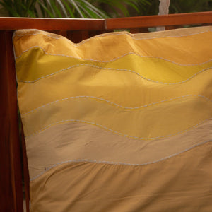 Yellow quilted pillow on a wooden chair with plants in the background
