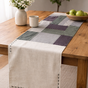 Checkered cotton table runner on a wooden table with a vase, mug, and bowl of apples.