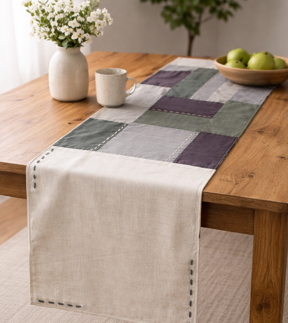 Checkered cotton table runner on a wooden table with a vase, mug, and bowl of apples.