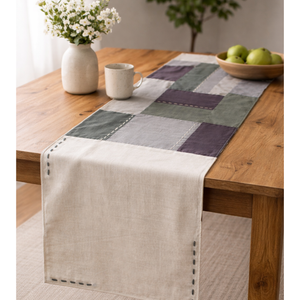 Checkered cotton table runner on a wooden table with a vase, mug, and bowl of apples.