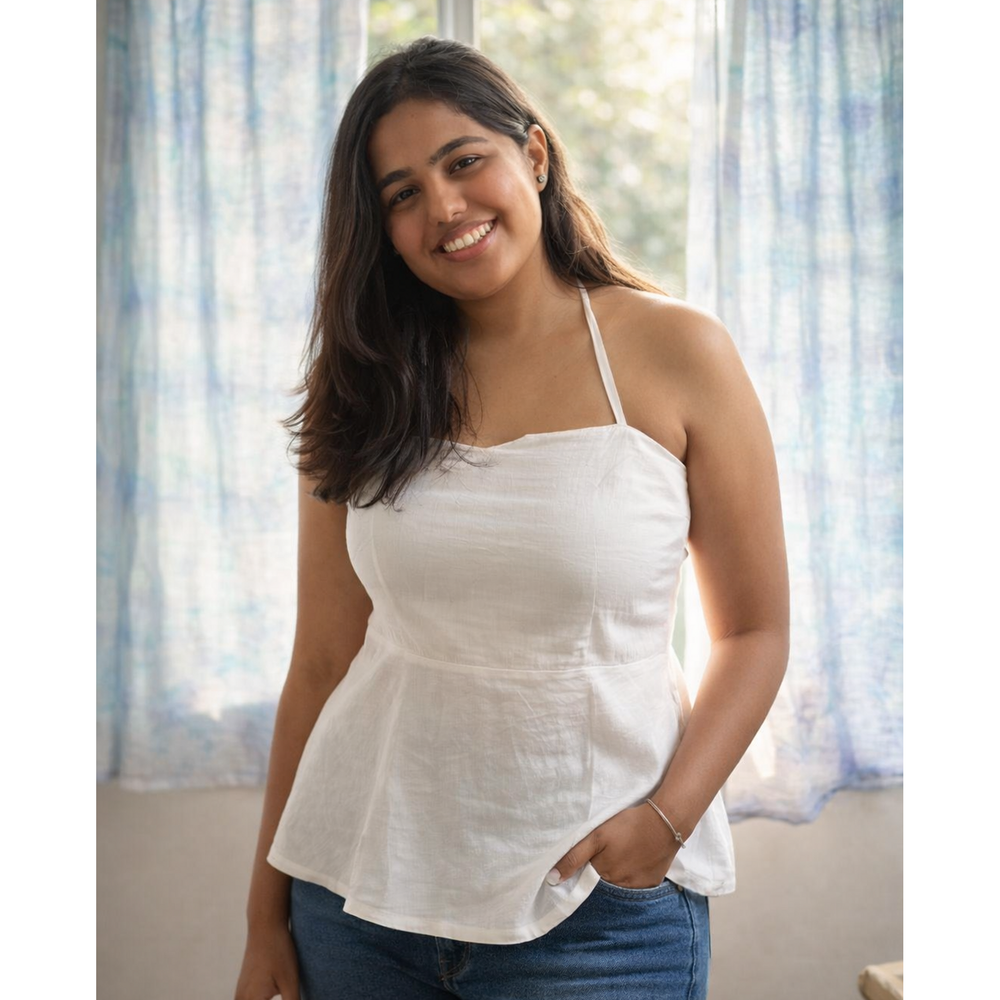 Woman wearing a white top and blue jeans standing in a room with light curtains.
