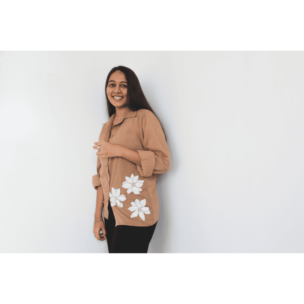 Woman wearing a beige shirt with white floral patterns on a plain background