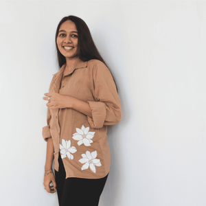 Woman wearing a beige shirt with white floral patterns on a plain background
